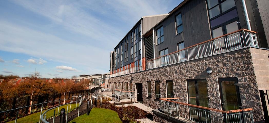 A fully accessible walkway around the rear of the property with views of the mature trees and grassed areas.