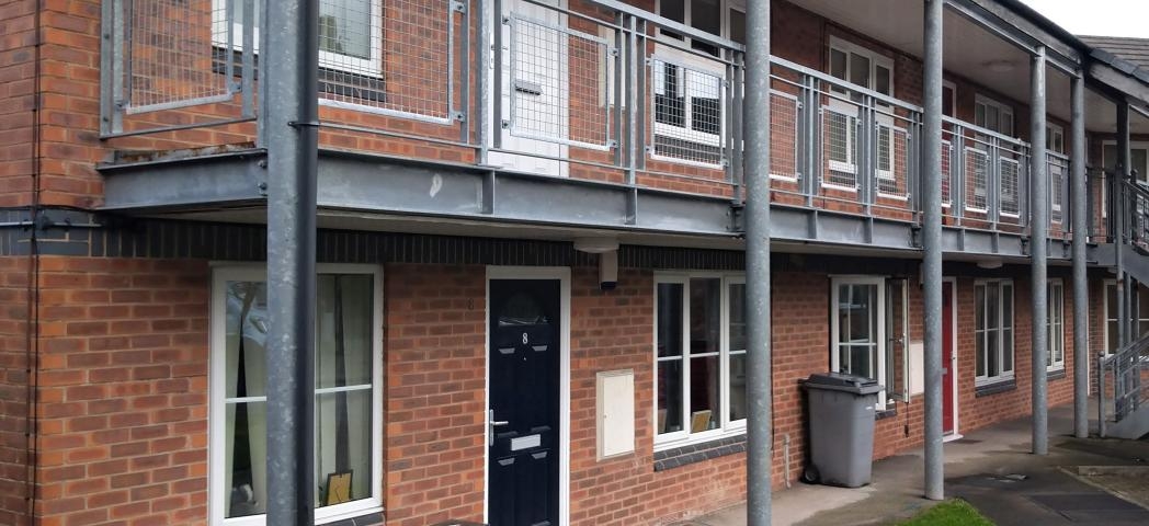 Industrial support metal beams and balcony on the second storey frame the entry to Thomas Court flats. 