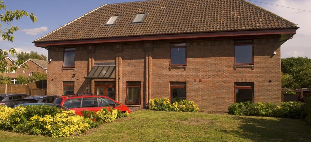 Red brick, flat topped roofed building with a lawn in front.