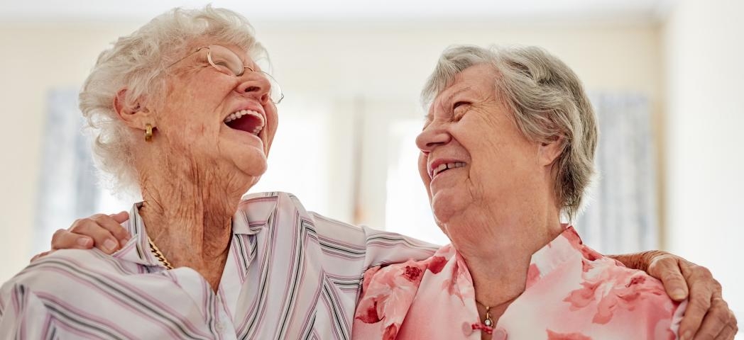 Two happy elderly women embracing each other at home
