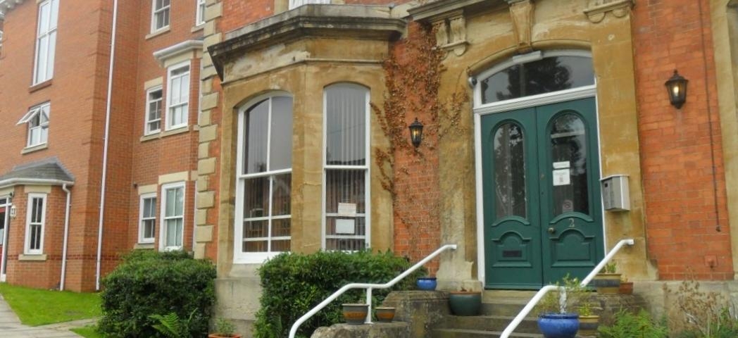 Exterior of a red brick terraced house with a bay window, a green double front door and steps leading down to a walkway