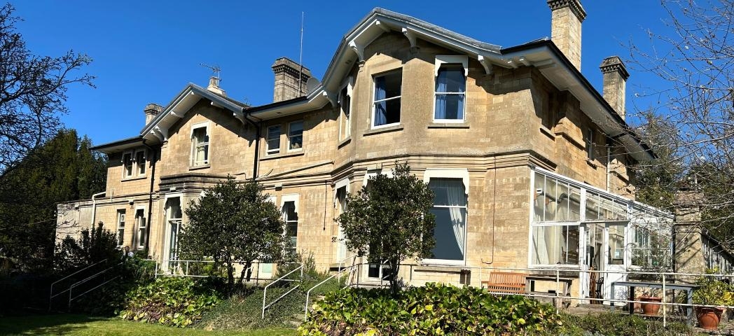A large cream-grey building with two floors, with a green lawn in front and blue sky.