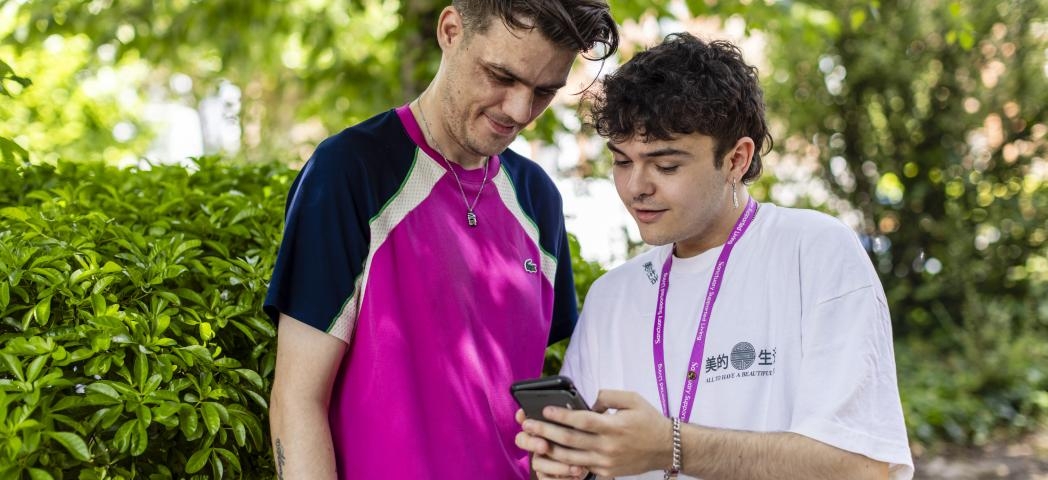 A Sanctuary Supported Living employee and a young male stood together looking at a phone outside in the sunshine