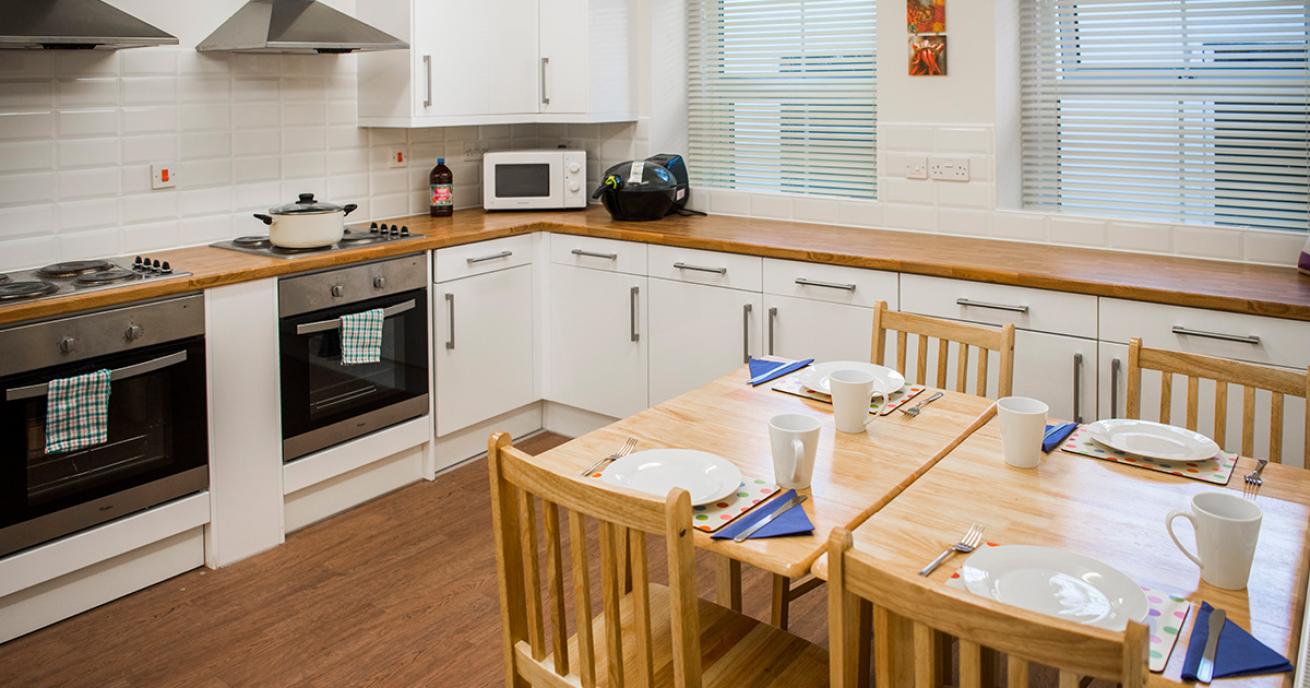 Classic kitchen. With white subway tiles and cupboards decor and wood finished work top, flooring and dining table. Alongside stylish appliances. 