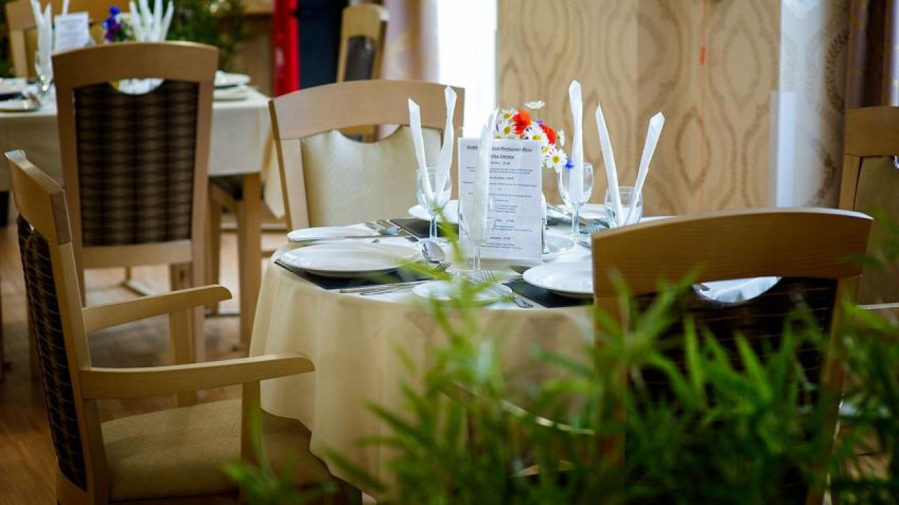 A beautifully presented dining table. Covered in a white pressed linen cloth, black mats, dining plates and side plates. Cutlery set for a three course dining experience and wine glasses with napkins. 