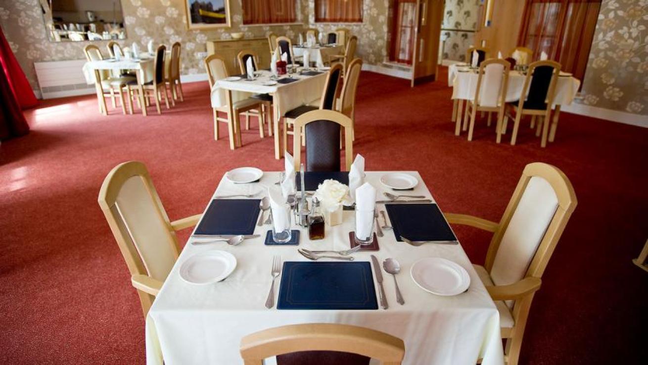 The spacious dining room is home to multiple dining tables dressed in white linen cloths and matching chairs with cream and aubergine coloured leather upholstery. The tables are dressed with leather placemats, silver cutlery. 