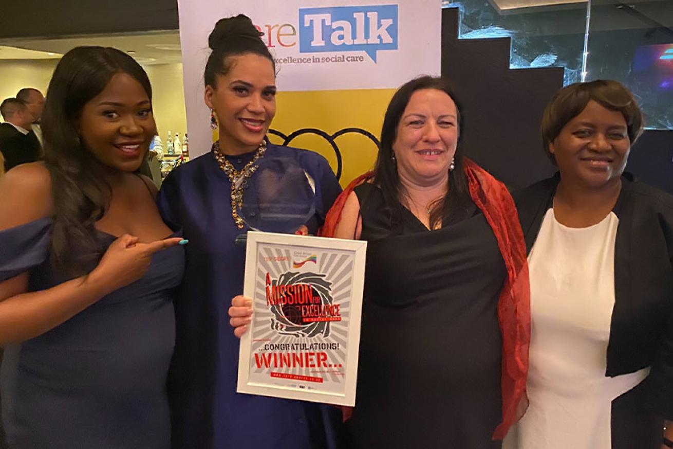 Award winner proudly holds her and stands with other Sanctuary colleagues, dressed up in smart attire.