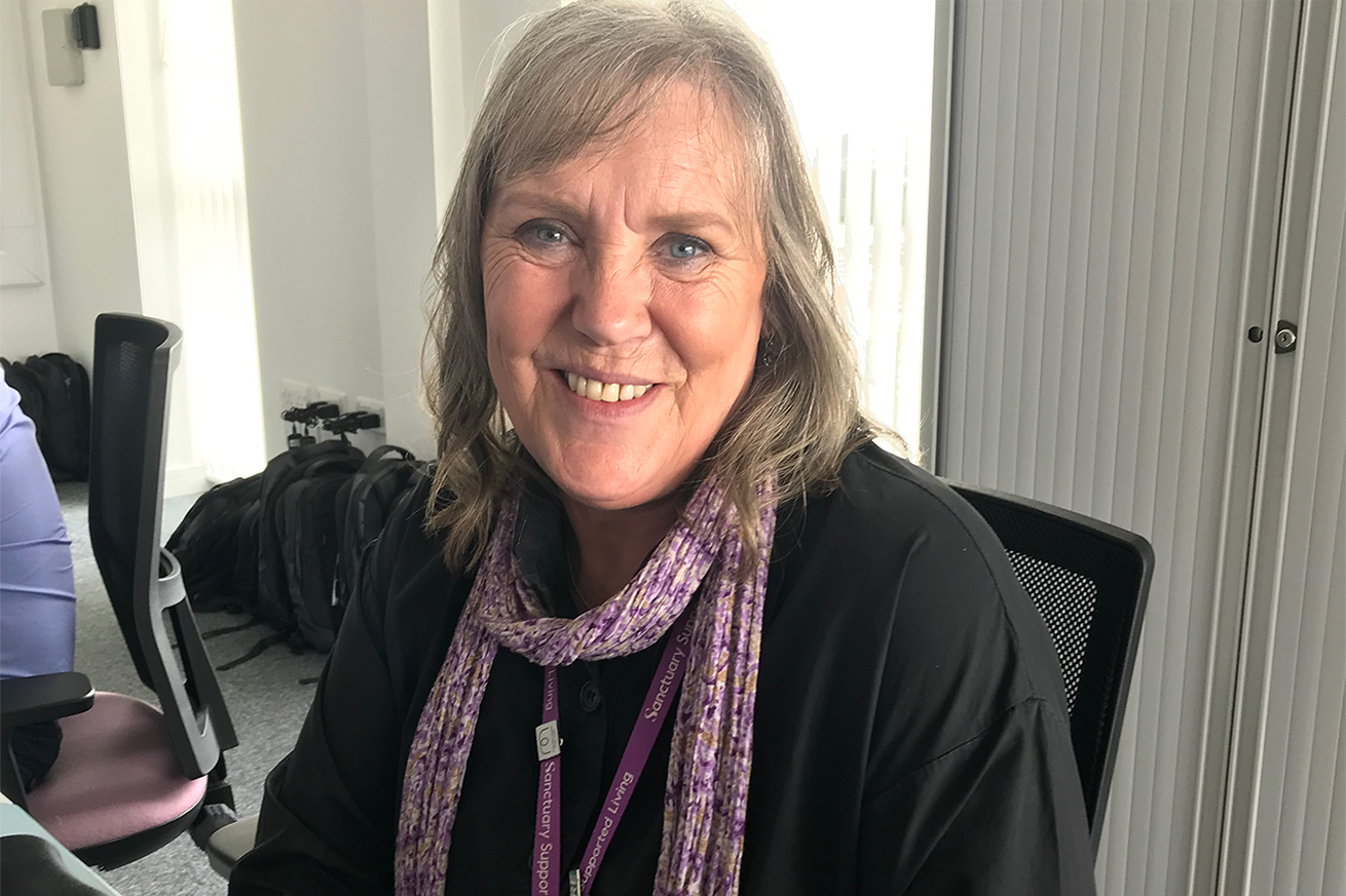 A Sanctuary Supported Living member of staff sat smiling at their desk