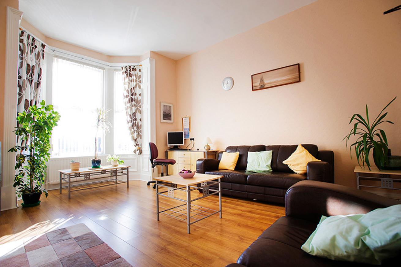 A naturally lit living room with peach coloured walls and a bay window. There are two sofas, a coffee table and large green plant by the window