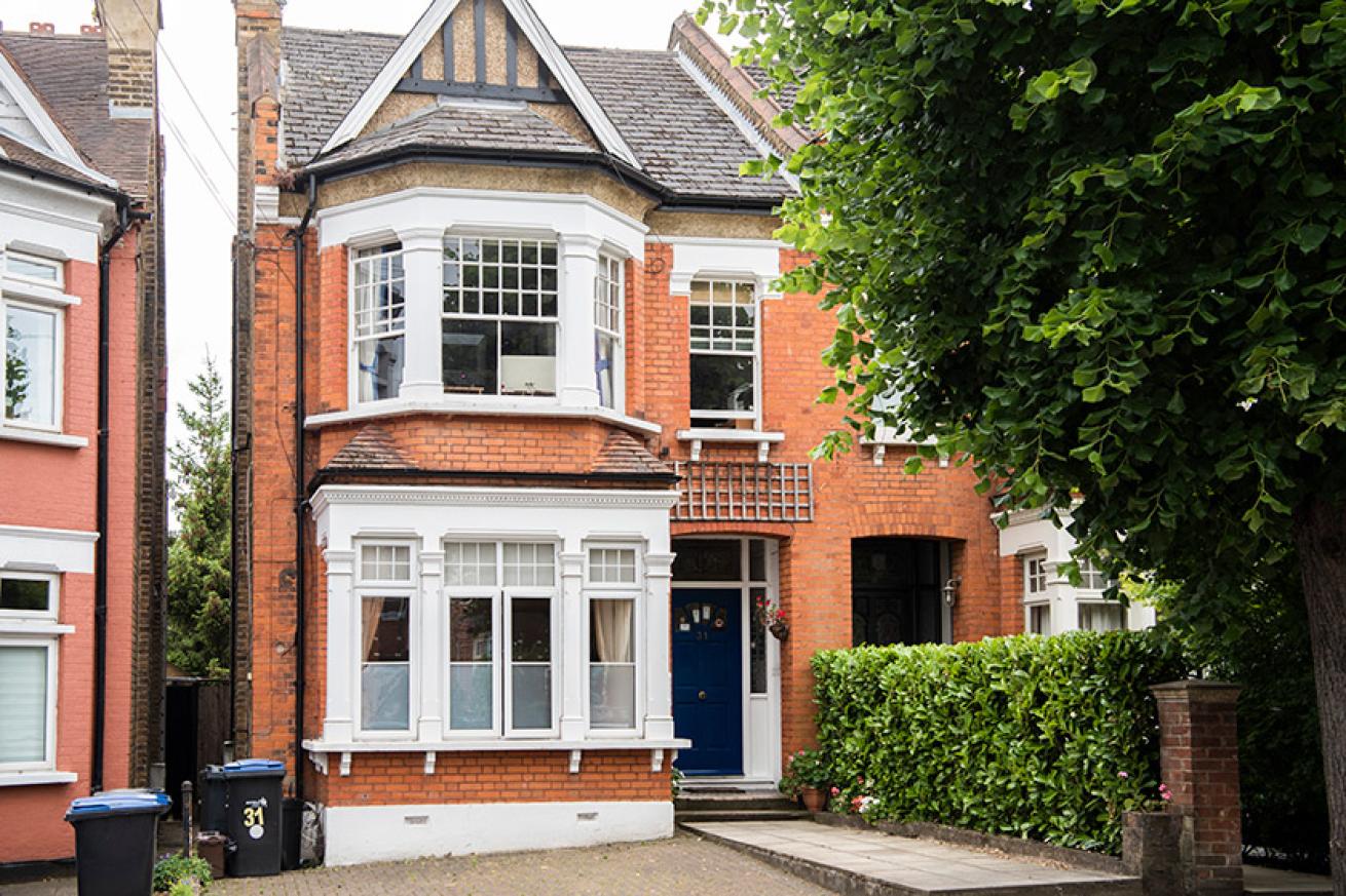 The exterior of the front of a red bricked house with bay windows