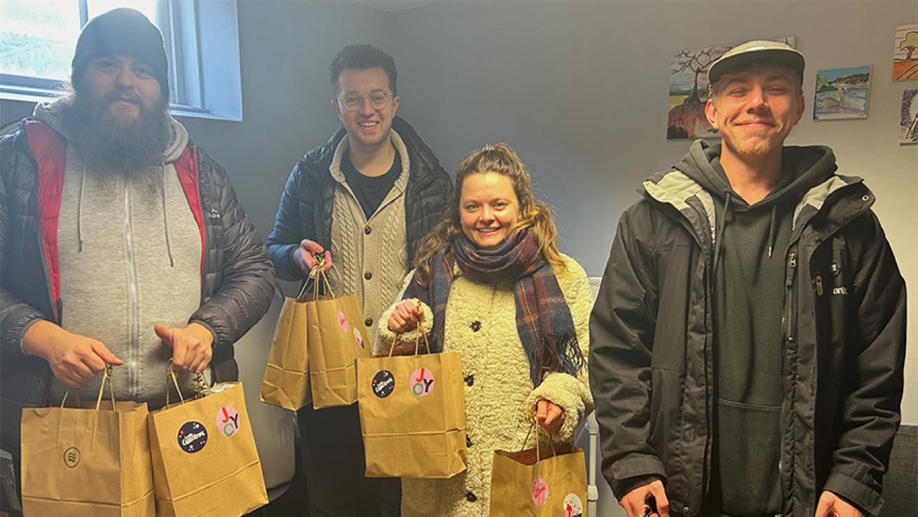Three men and one woman stood holding brown paper gift bags, smiling at the camera