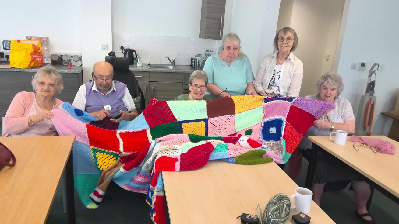 Residents at Jazz Court proudly displaying the kitted blanket they have made for a charity raffle