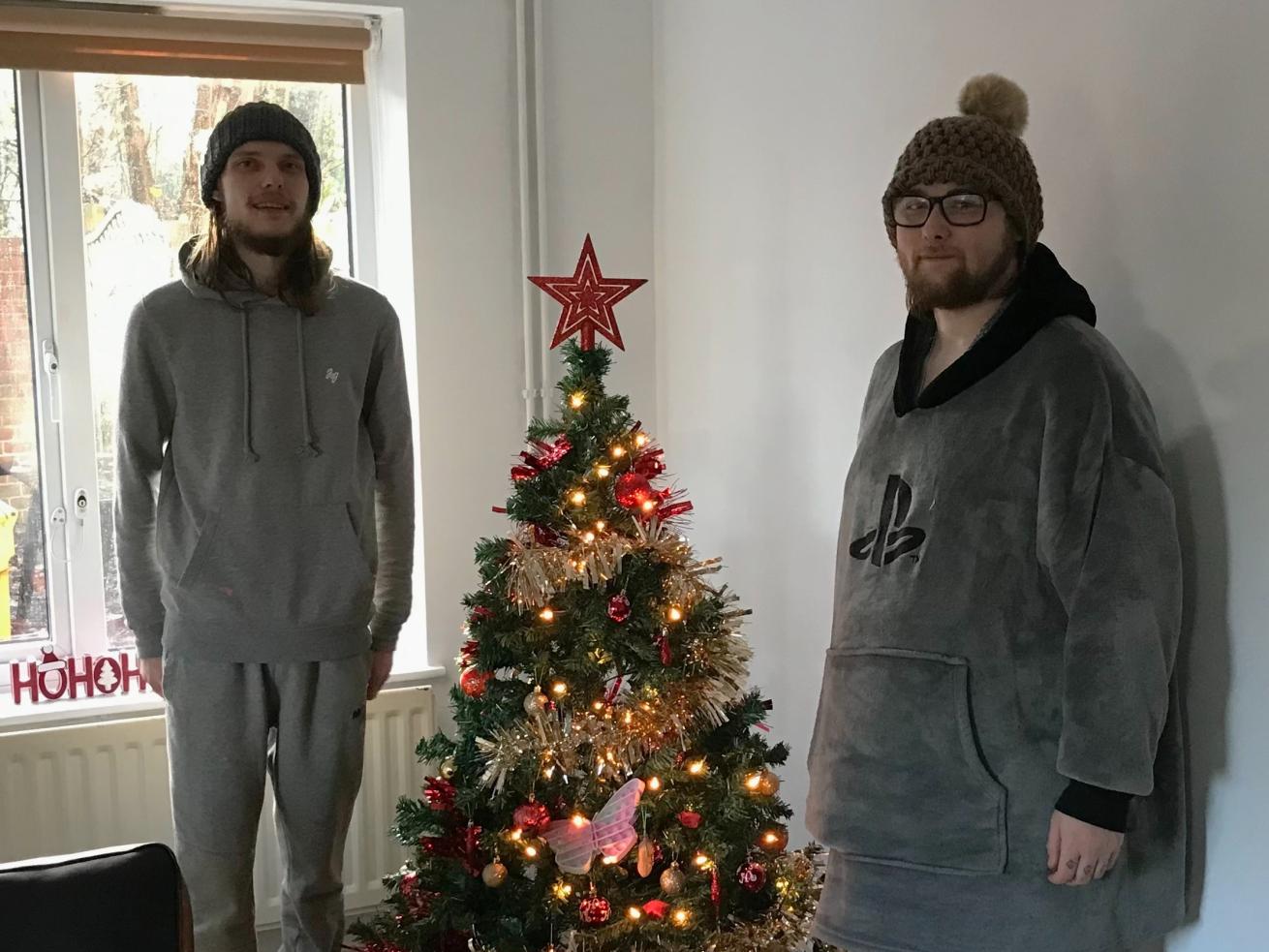 Two residents at Sudbury Young People Supported Housing wearing winter hats in front of a decorated Christmas tree