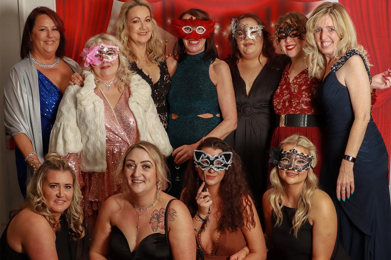 TDAS staff posing for a photograph in their glamorous outfits at a masquerade ball to raise money in support of their work. Several of the ladies pictured are wearing glittery masks.