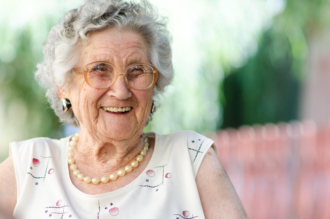 An elderly lady wearing a white top and pearl necklace smiling and looking off camera