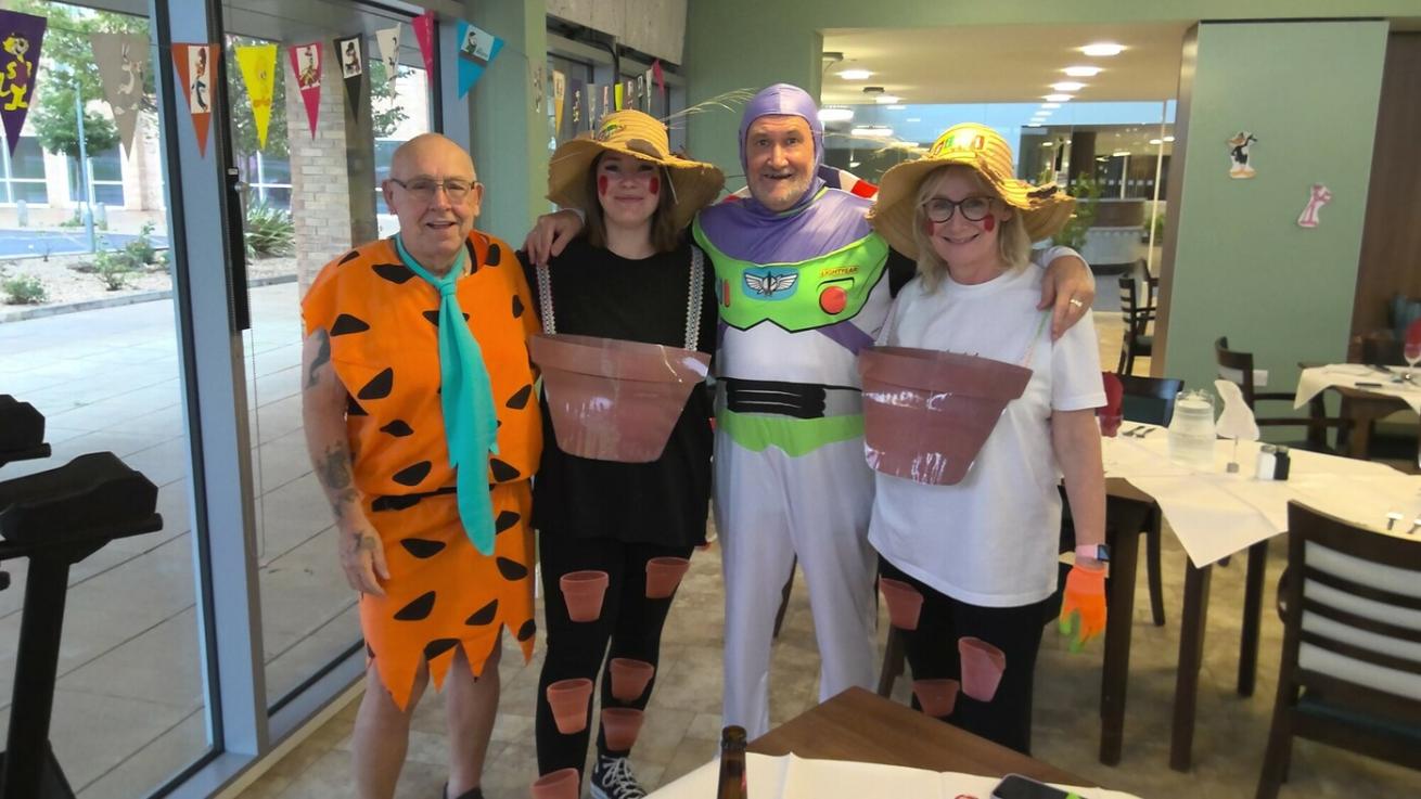 Two women and two older men all dressed up, stood together and smiling at the camera. One man is Fred Flintstone, the other is Buzz Lightyear and the two women are Bill and Ben the Flowerpot Men.