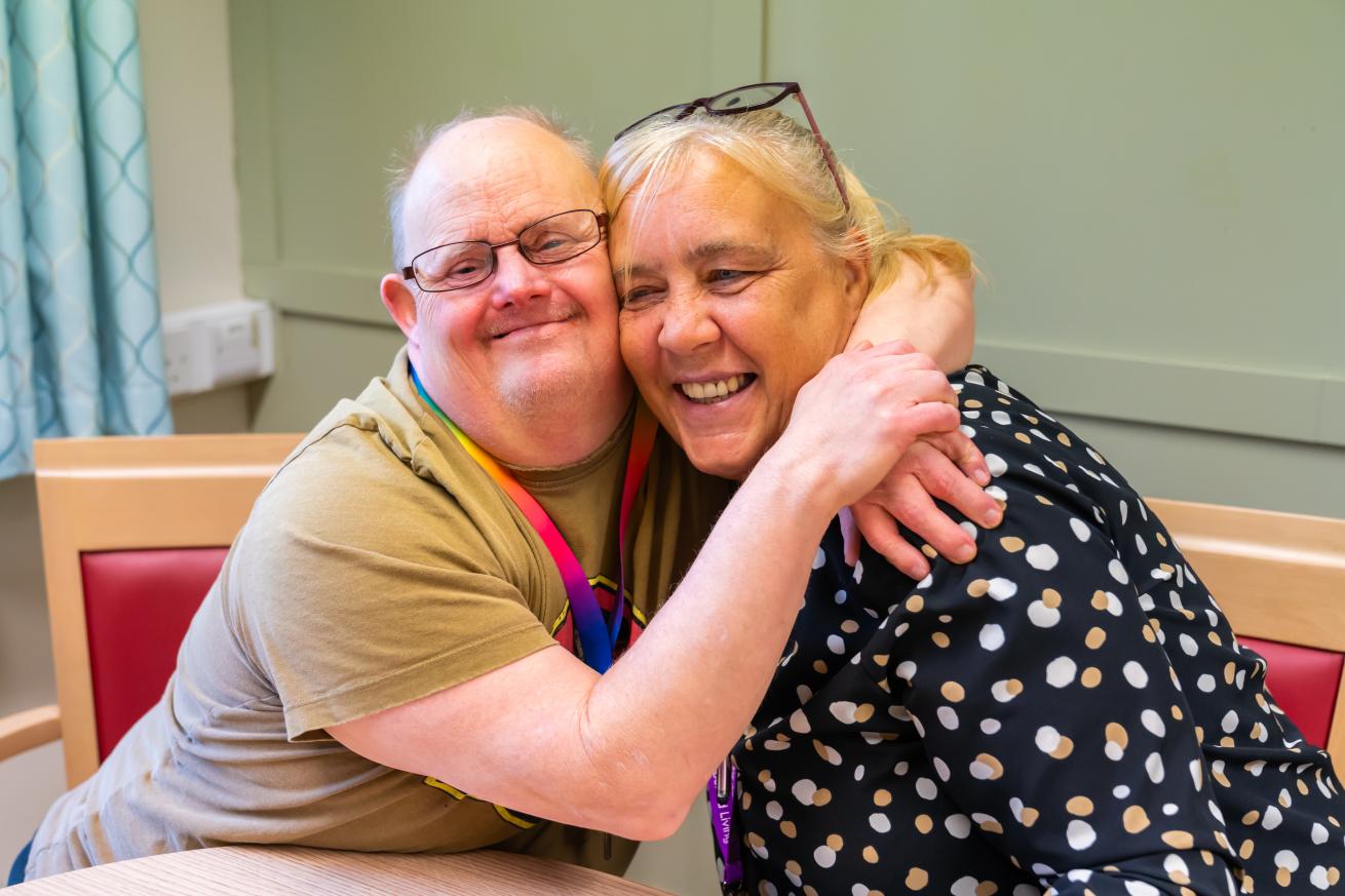 Two people sat at a table smiling and embracing