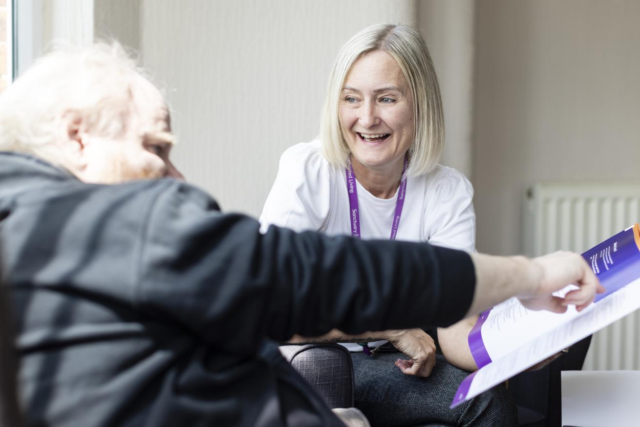 A staff member is smiling while holding a book while a resident points to it
