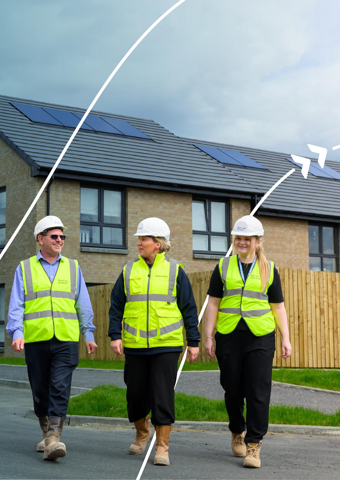 Three people wearing high-visibility clothing and hard hats walking through a residential housing development with solar panels on the roofs.