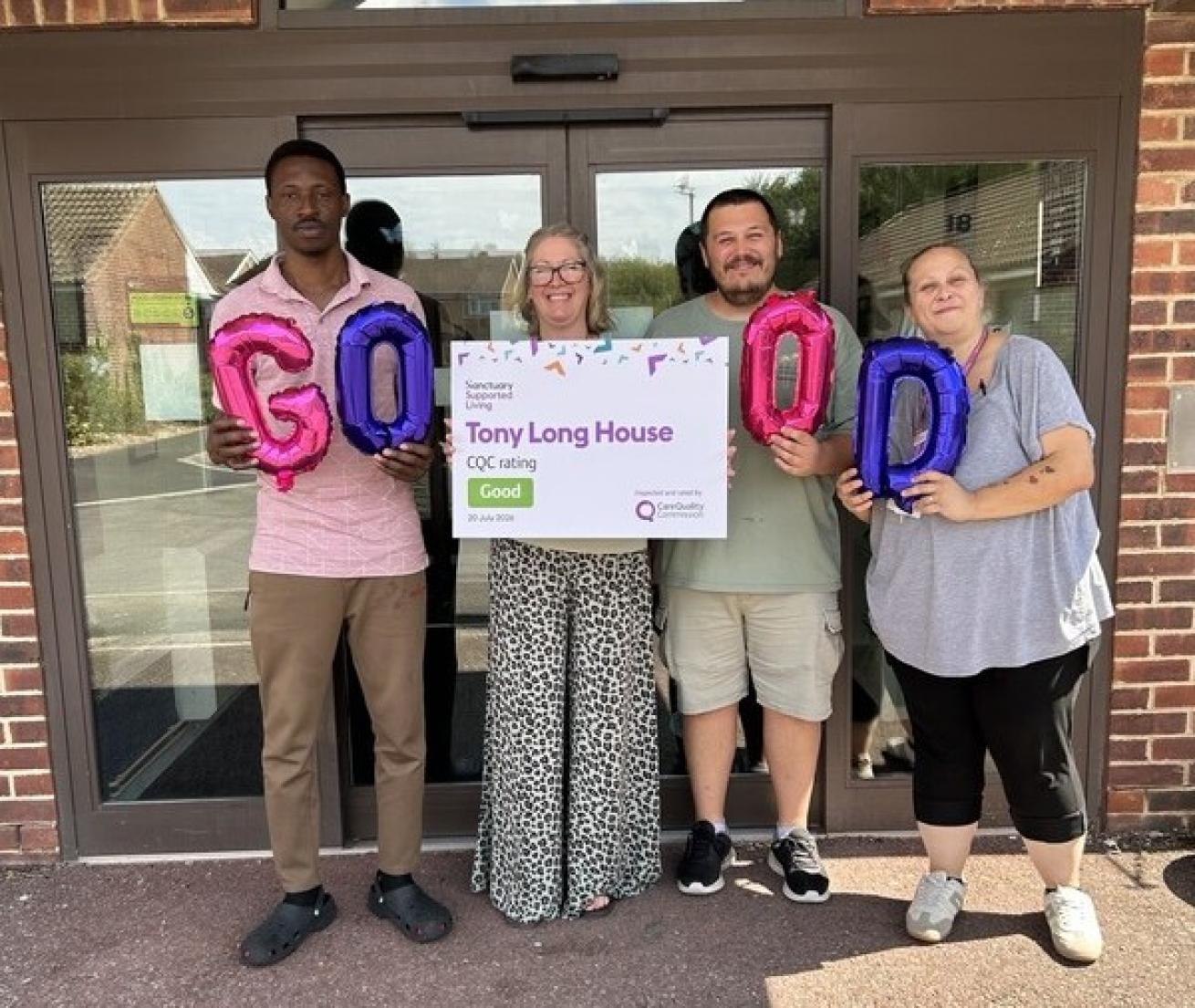 Four individuals stand in front of a building, holding balloons that spell "GOOD" and a sign with a "Good" CQC rating for Tony Long House.