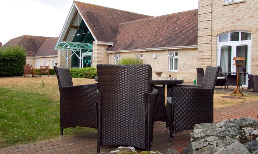 Two outdoor charcoal wicker dining sets are placed amongst the bricked walkways surrounding the grassed area. 