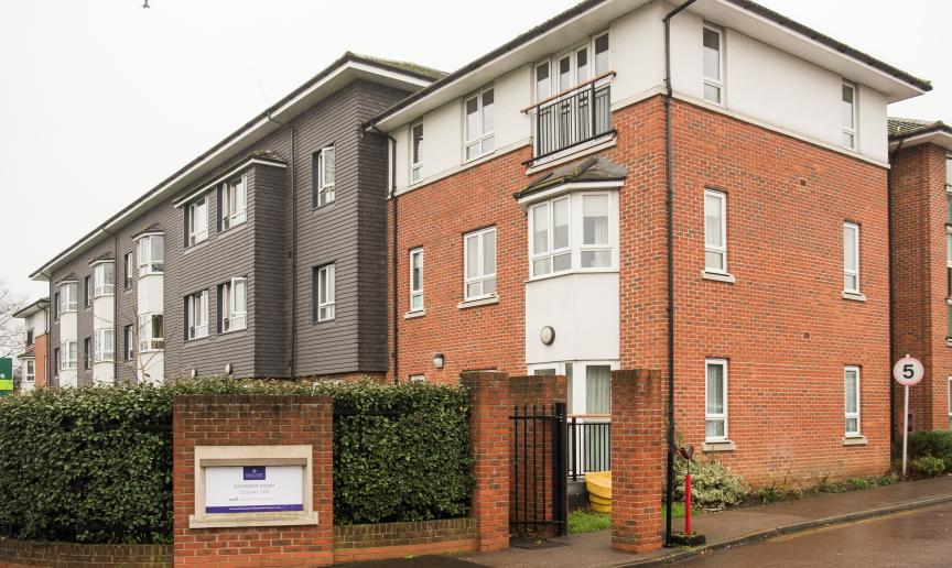The newly built brick, three storey retirement community. With a large hedge wrapping the front of the property for privacy, an iron gate for pedestrians and a speed restricted driveway.  