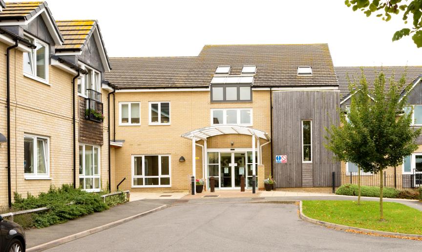 A modern two storey property built with yellow brick and a wooden panelling in random locations on the exterior of the property. The entrance has a covered walkway and dropped curb access. 