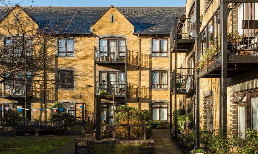 Traditional yellow bricked property with grey bricked framing around the windows and doorways. Iron barred balconies are attached to the large curved toped patio doorways. Wheelchair access pathways run around the perimeter of the building.