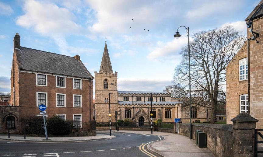 St Peters Church in Mansfield town centre with vicarage and one way road passing through village.