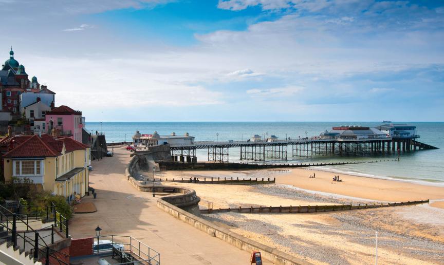Large promenade walkway leading to a modern pier which features over a mixture of sand and stone beach and into the North Sea.