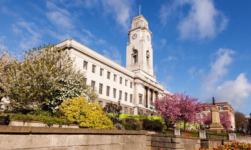 Stone built town hall with well-maintained gardens in bloom.