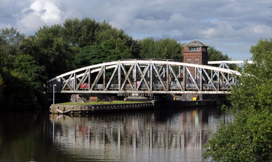 Weathered silver, curved metal bridge creating access over the river.