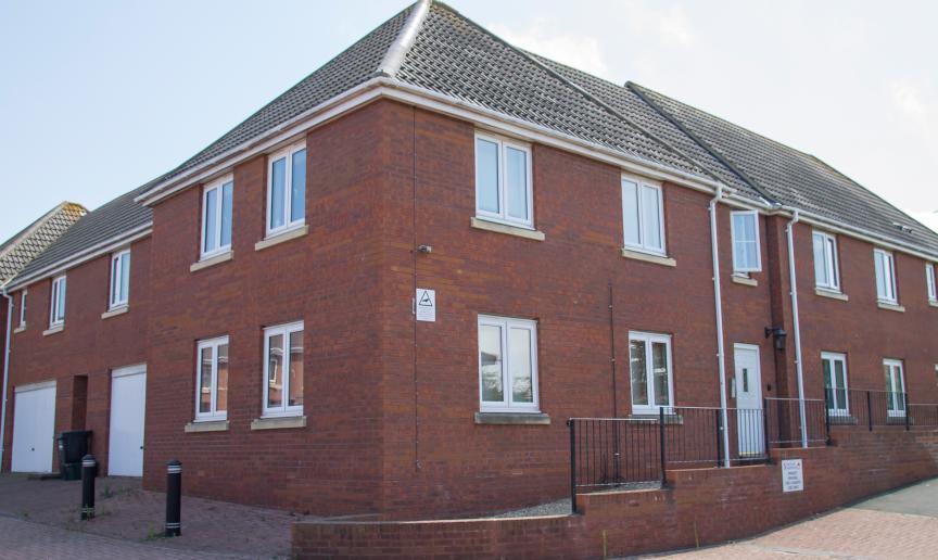 New build, red brick corner plot with new white PVC windows, doors and garage. A bricked wall surrounds the walkways. 