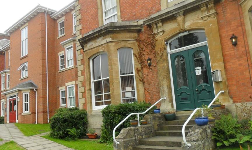 Victorian styled, three storey property with protruding bay windows and an array of forest green and red double entrance doors. 