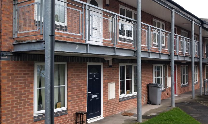 Industrial support metal beams and balcony on the second storey frame the entry to Thomas Court flats. 