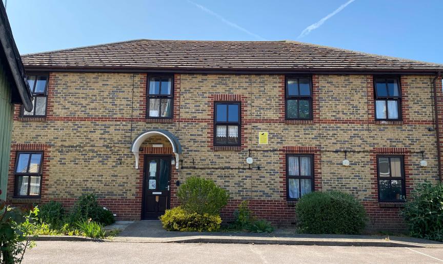 Traditional, elongated, two storey brown bricked property with decorative red brick design around the windows and entrance door. Small, well maintained shrubbery lines the perimeter of the property.