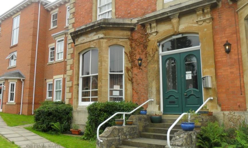 Exterior of a red brick terraced house with a bay window, a green double front door and steps leading down to a walkway