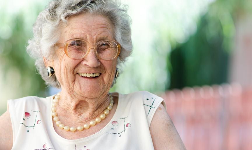 An elderly lady wearing a white top and pearl necklace smiling and looking off camera