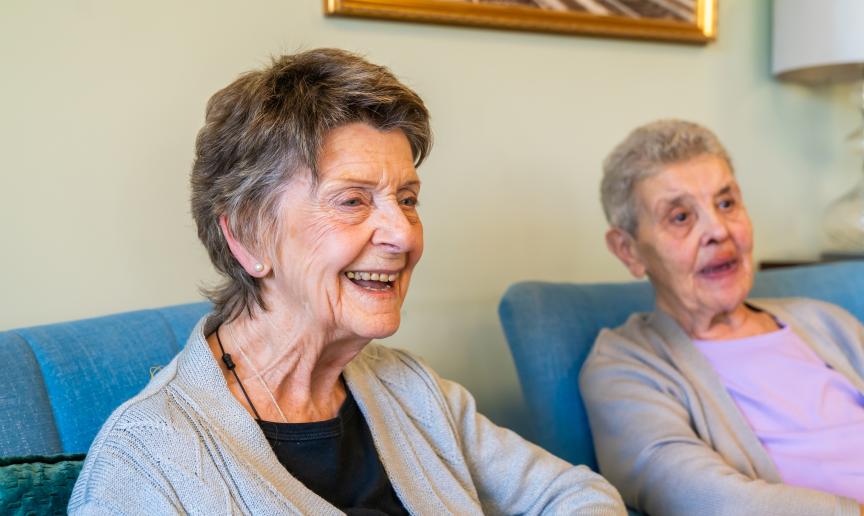 Two elderly women sitting on blue armchairs looking off camera and smiling