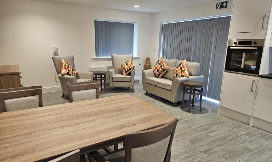 Interior of a communal area with neutral tones, a three piece suite and a wooden table surrounded by chairs at Silverbirch View
