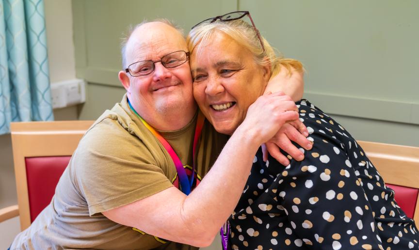 Two people sat at a table smiling and embracing