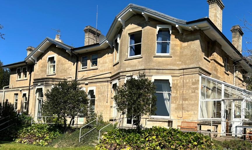 A large cream-grey building with two floors, with a green lawn in front and blue sky.
