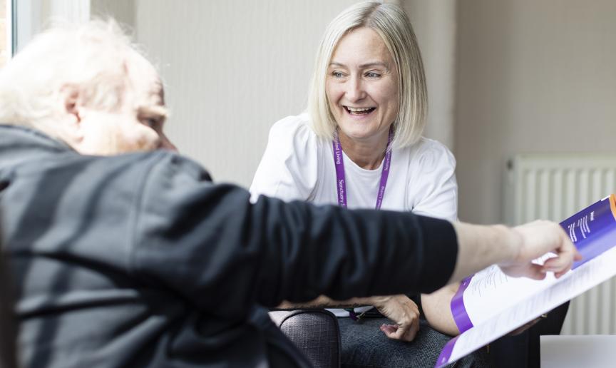 A staff member is smiling while holding a book while a resident points to it