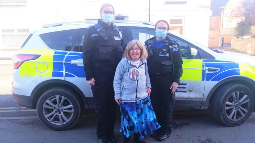 PCSOs from Cleveland Police with resident, who is wearing a 70th birthday badge, standing in front of a police car