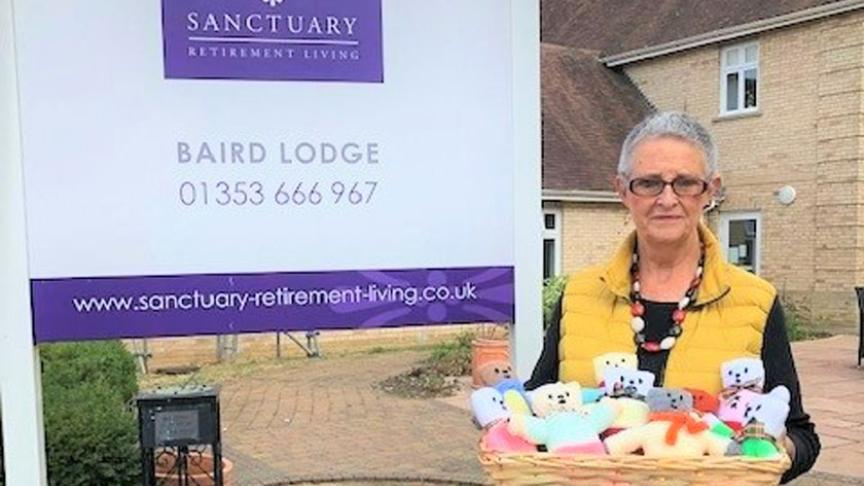 Sanctuary staff member standing outside Baird Lodge with a basket of knitted teddies