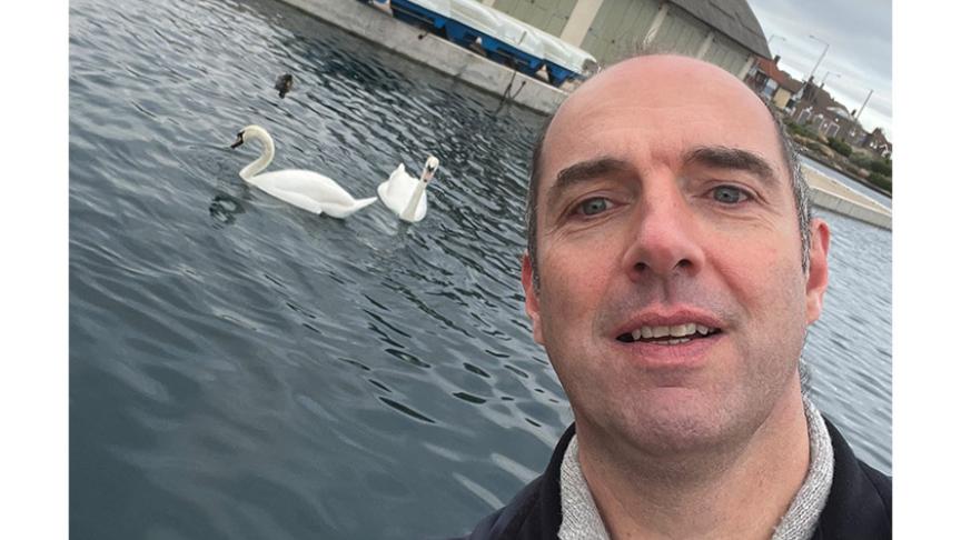 Project Worker posing with two swans swimming behind him