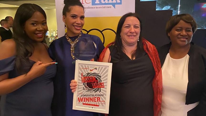Four Sanctuary staff members standing in front of a banner at the awards ceremony, the winner holding her award and certificate proudly