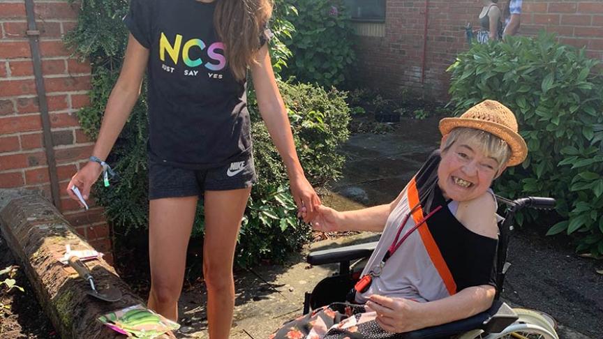 NCS gardening volunteer holds hands with a resident, who is a wheelchair user, in the garden