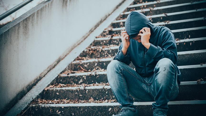 Stock image of a young man sitting on some steps holding his head in his hands