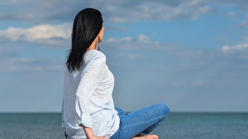 Stock image of a woman sitting on a pebble beach looking out to sea